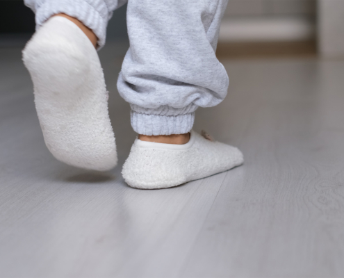 Legs of a woman in white socks walking on the wooden floor of her house